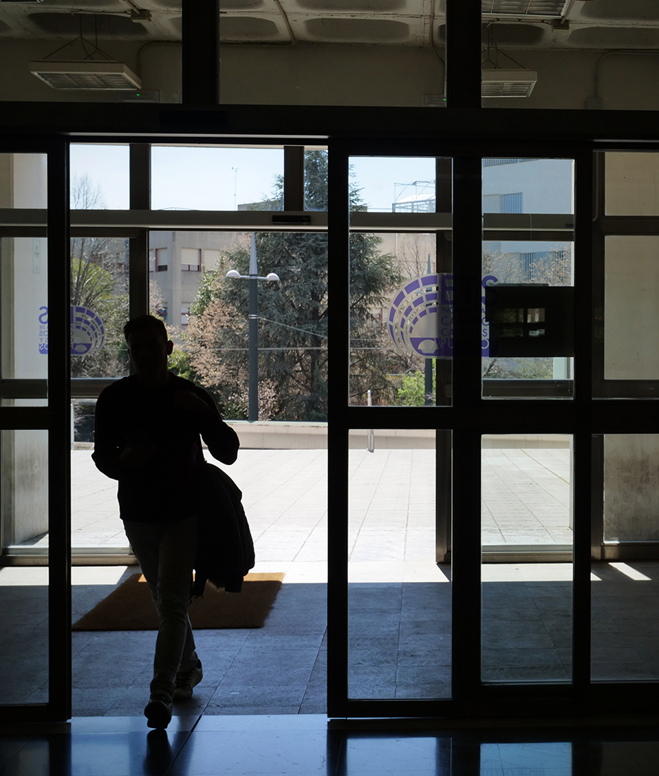 Estudiante de espaldas saliendo a la calle a través de la puerta central del edificio Politécnico con detalle de vinilos de la ETS de Ingeniería de Caminos, Canales y Puertos